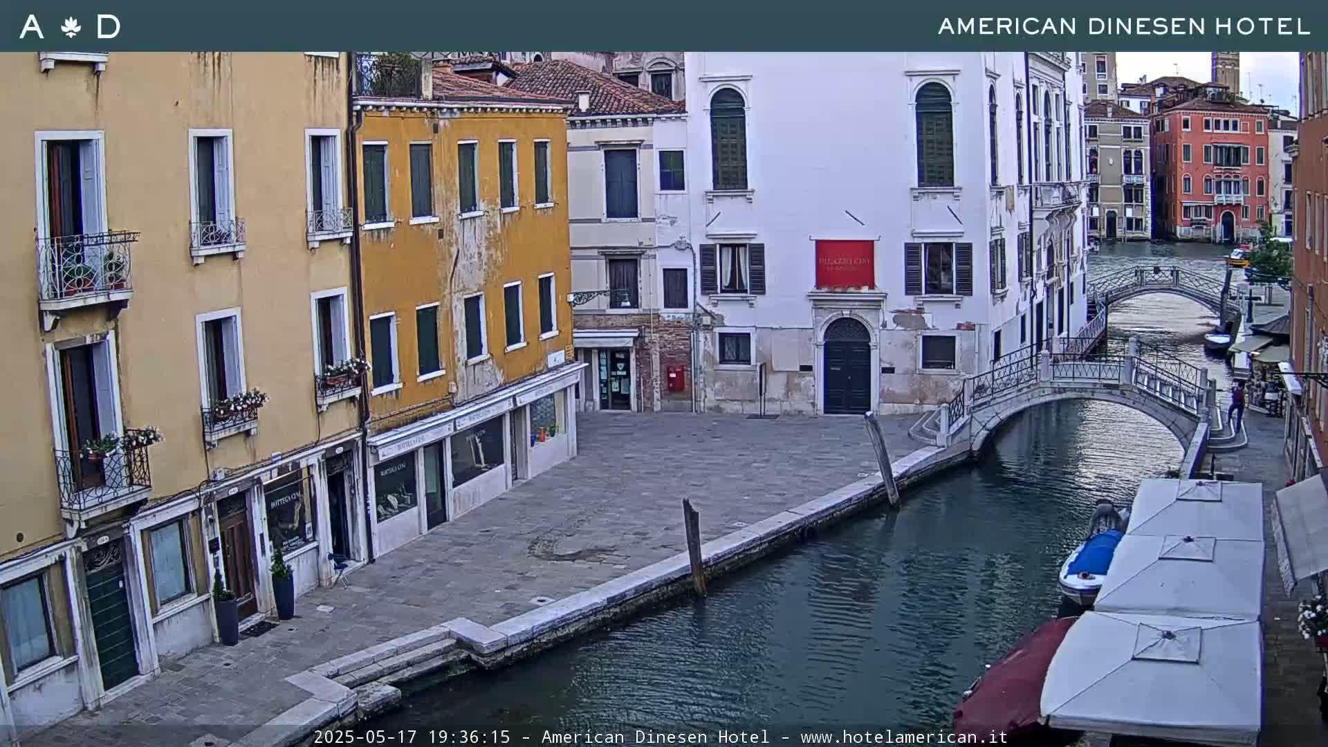 A canal in Venice, Italy, with several buildings lining the waterway and a small footbridge spanning the canal, under overcast skies.