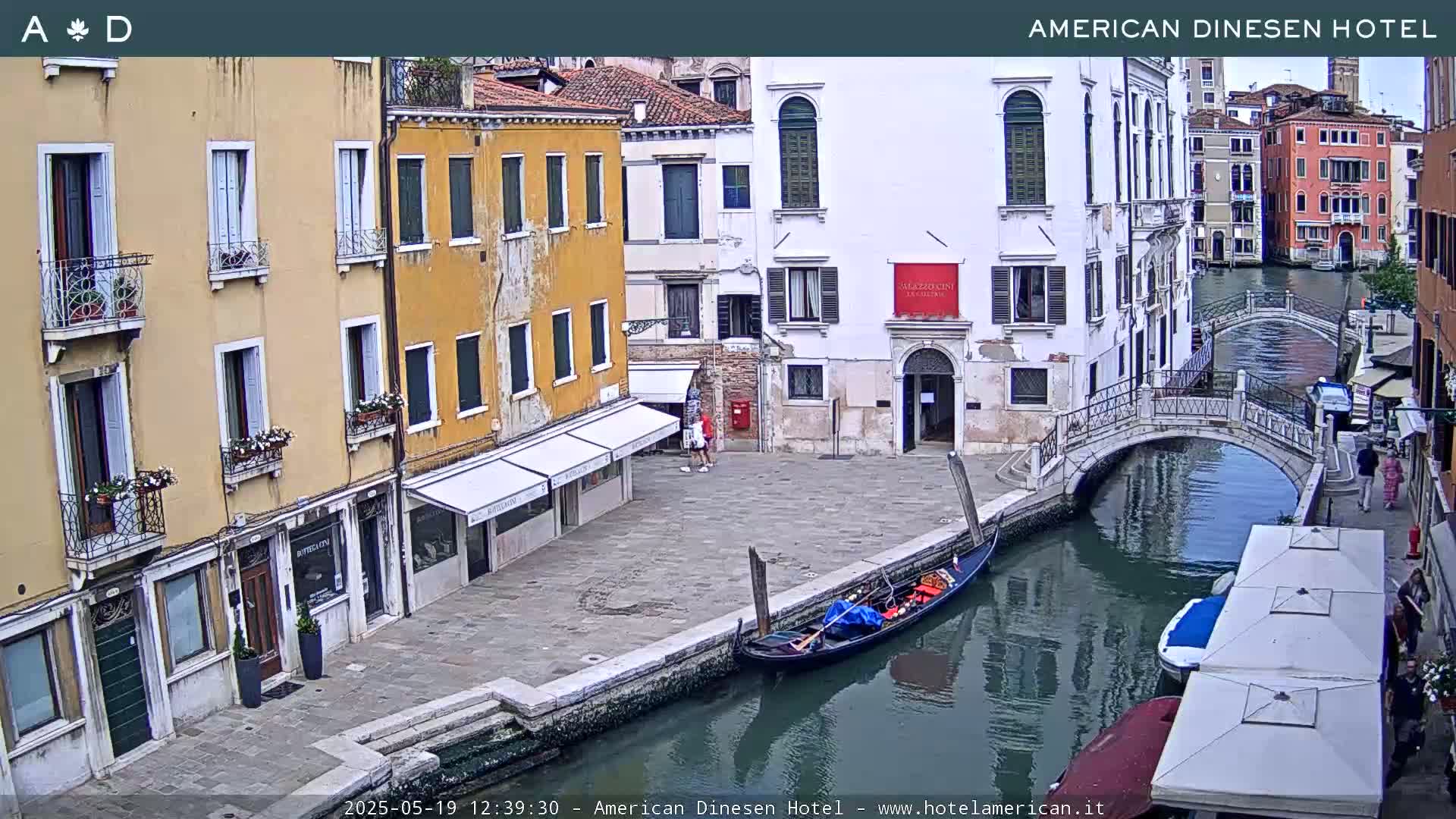 A gondola is moored along a canal in Venice, Italy, with several buildings lining the waterway under a partly cloudy sky.