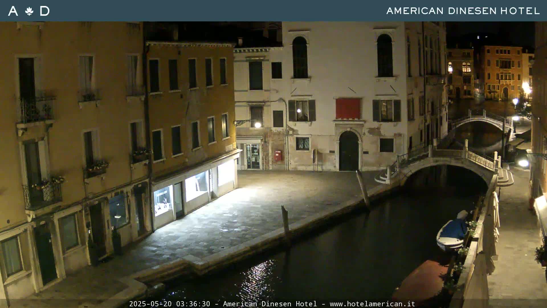 A nighttime view of a canal in Venice, showing several buildings and a small bridge, with a boat moored alongside the canal.