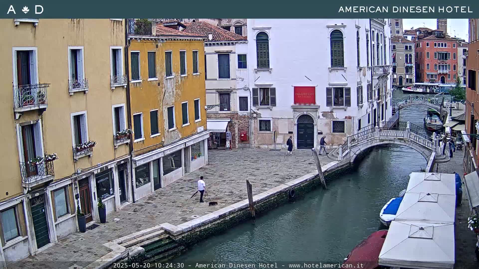 A canal in Venice, Italy, with several buildings lining its banks and a pedestrian bridge crossing it, under overcast skies.