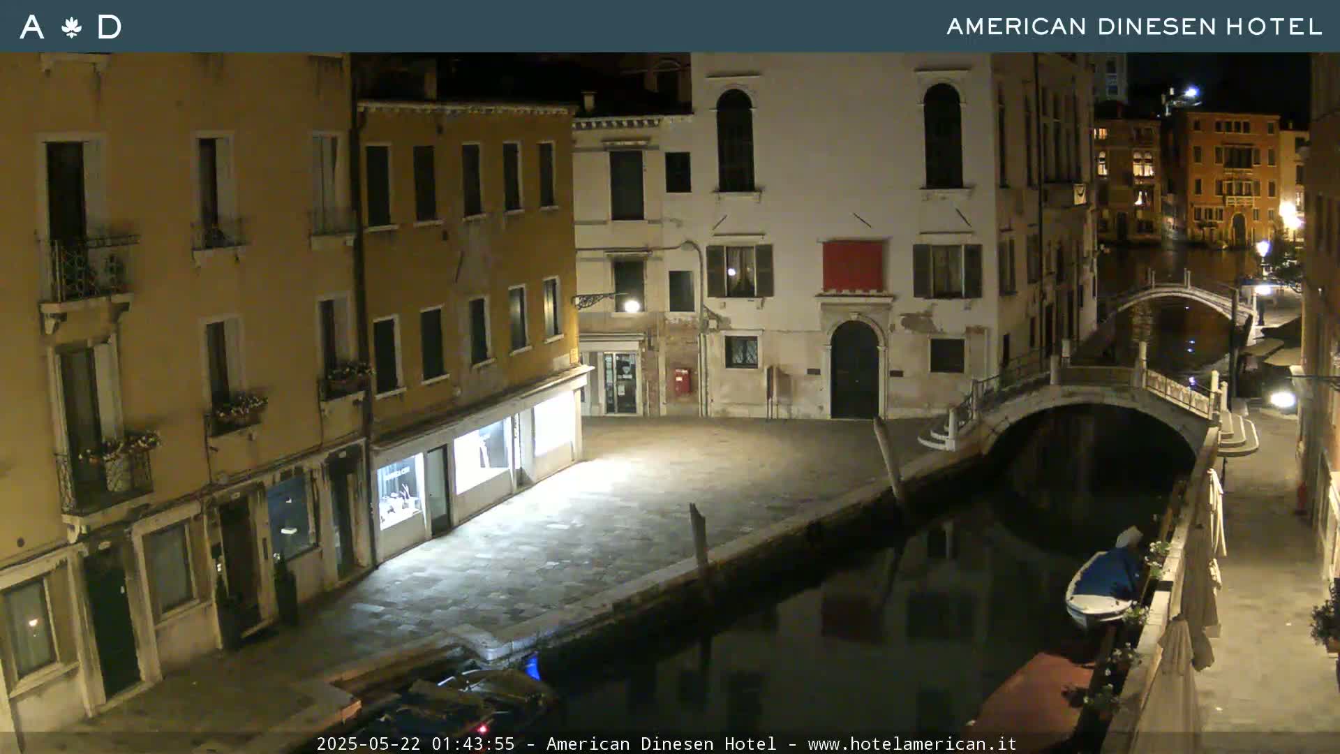 A nighttime view of a canal in Venice, Italy, shows buildings lining the waterway, a small bridge, and a boat moored alongside a wall.