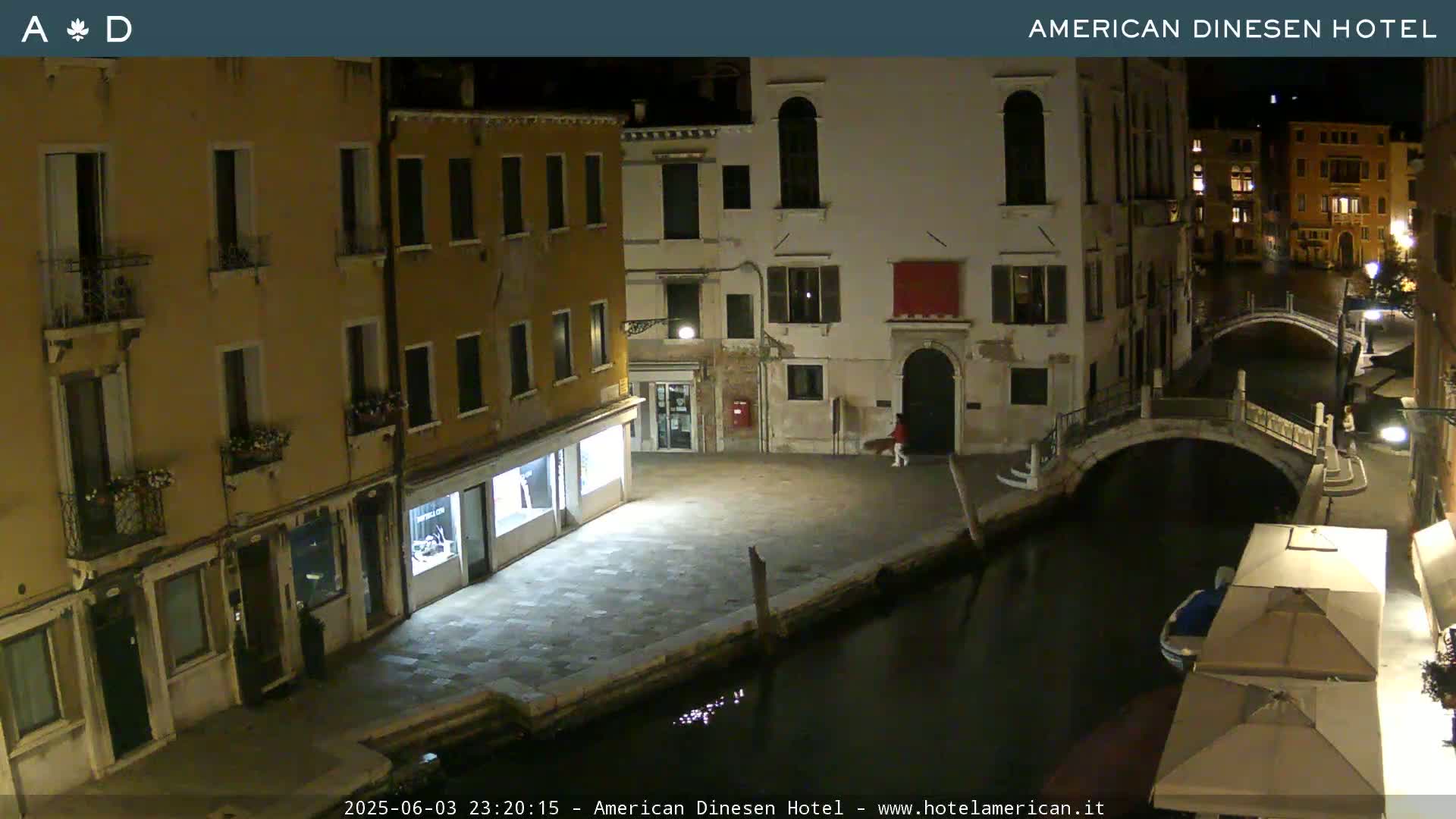A nighttime view of a canal in Venice, with buildings lining the waterway and a small bridge visible.