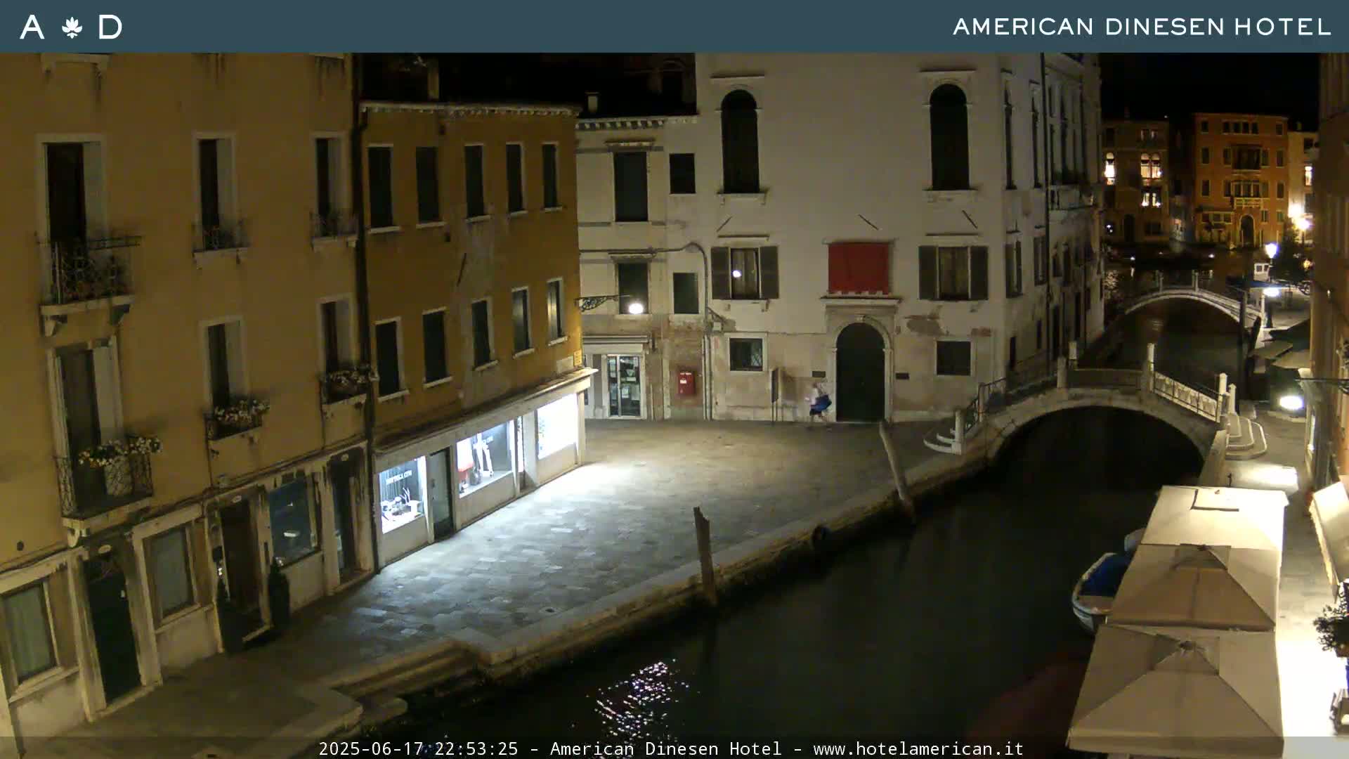A nighttime view of a canal in Venice, with buildings lining the waterway and a bridge visible in the distance.