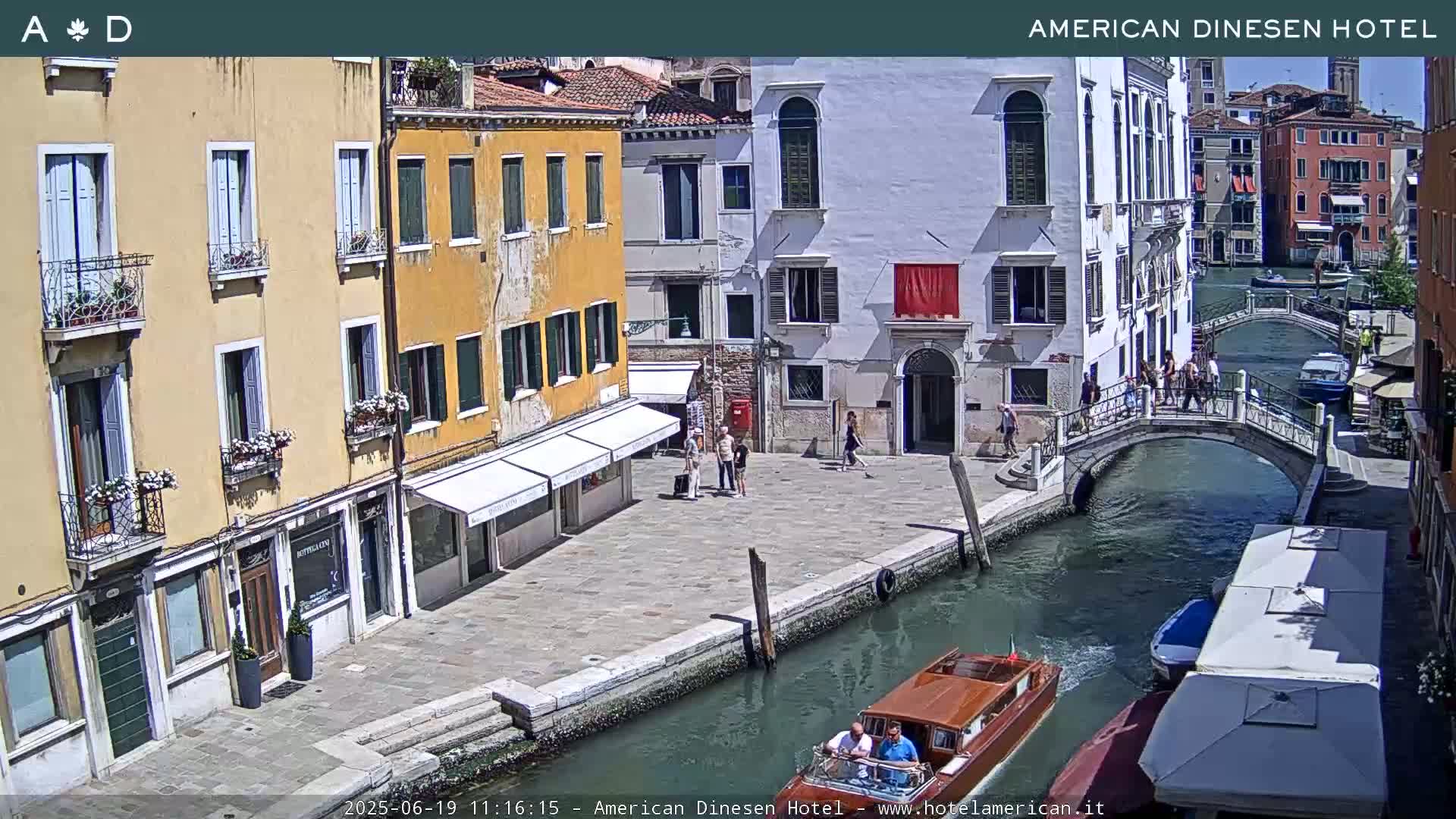 A sunny view of a Venetian canal with a wooden boat, pedestrians on a bridge, and colorful buildings lining the waterway.