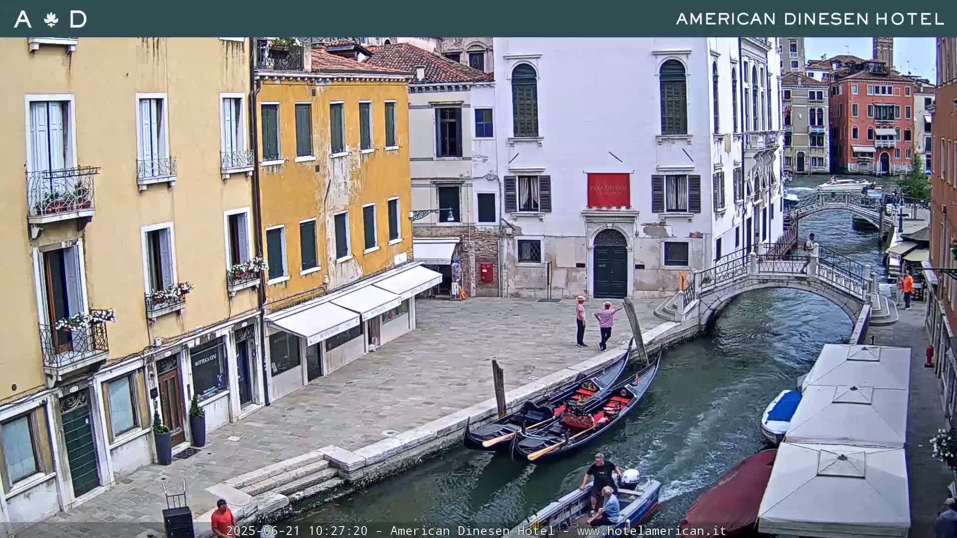 A Venetian canal scene shows gondolas moored alongside a bridge and buildings lining the waterway on a sunny day.