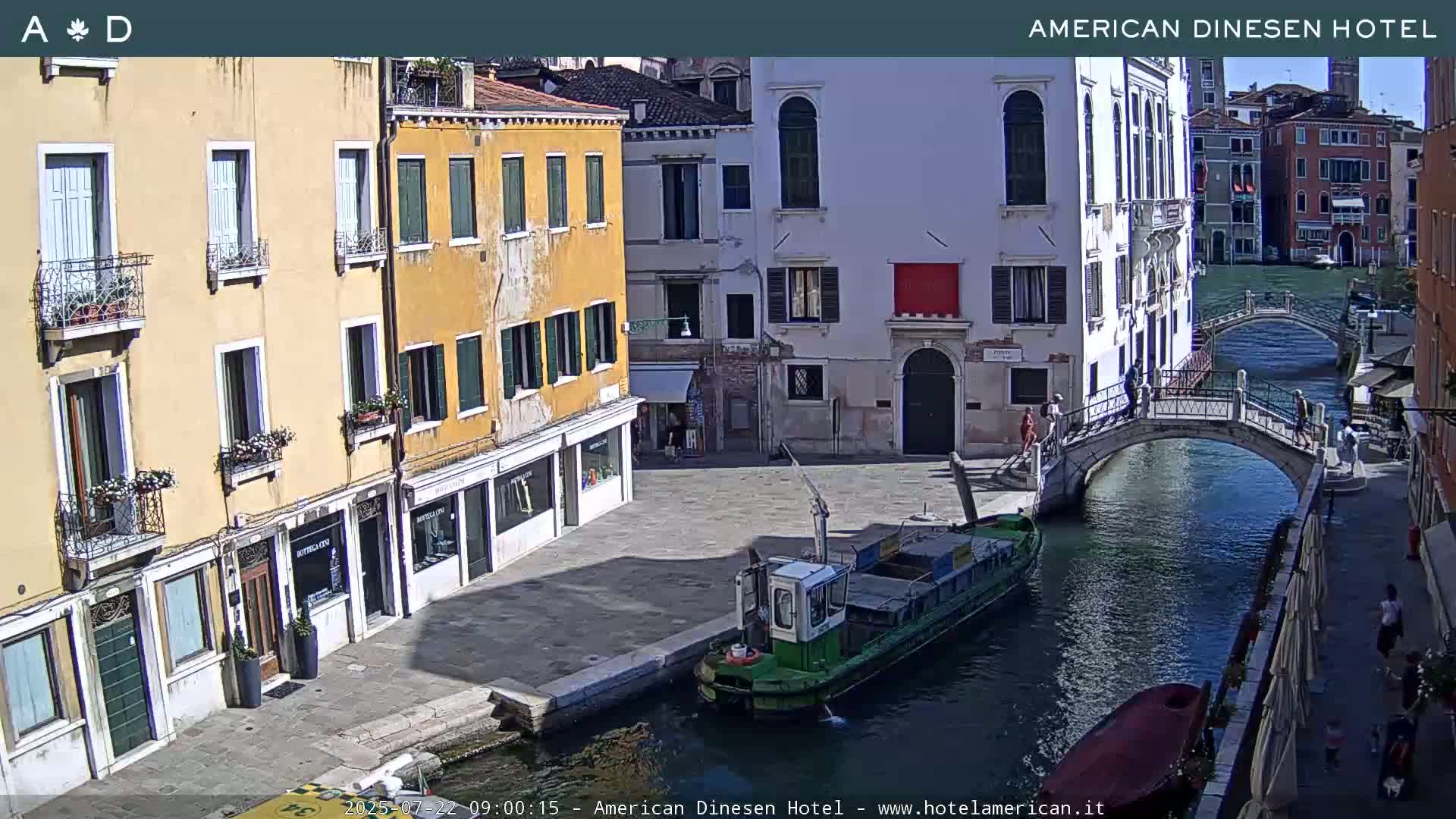 A sunny day in Venice shows a canal with a barge, a bridge, and colorful buildings lining the waterway.