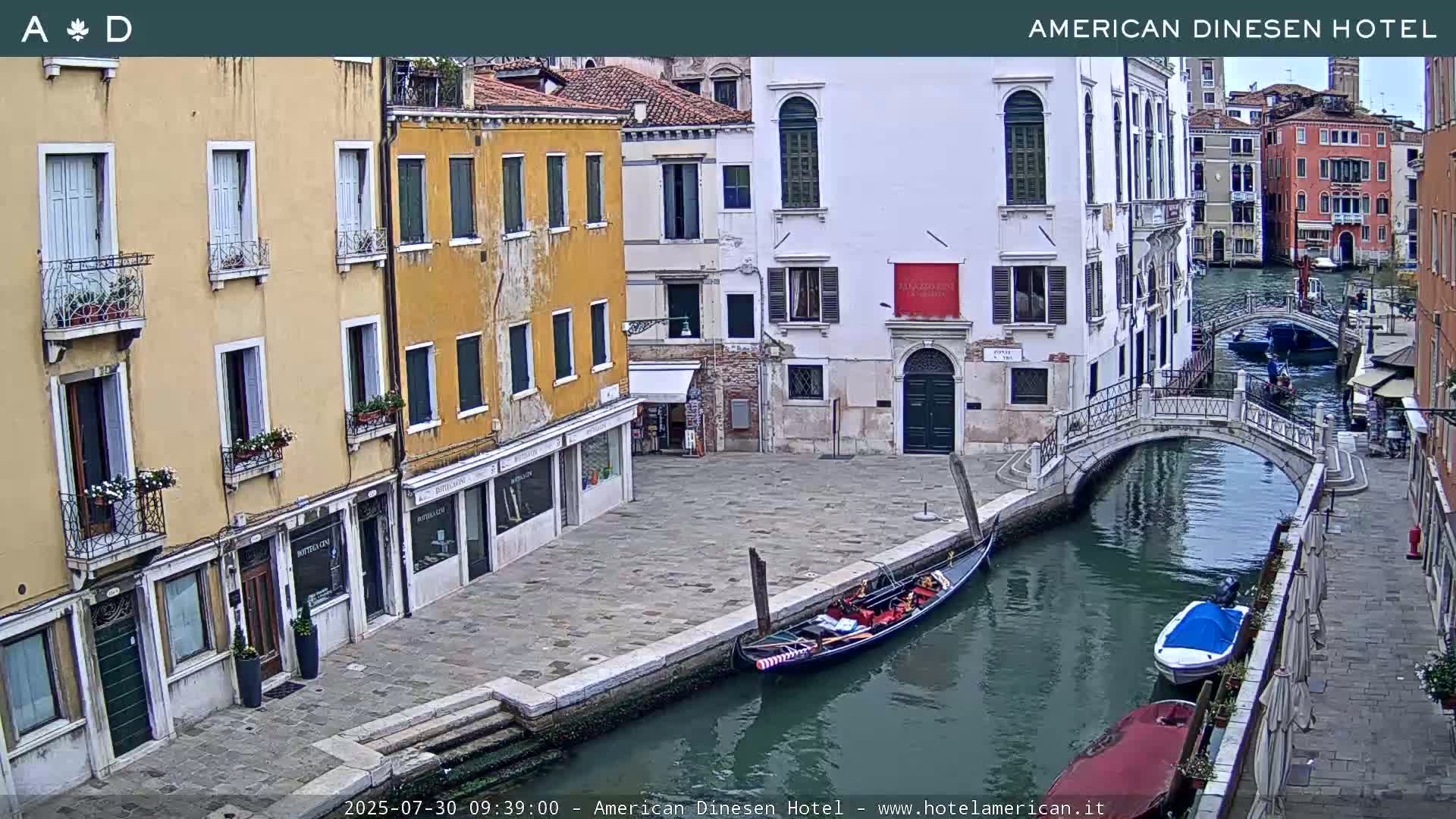 A gondola is moored in a canal beside buildings in Venice, with a small bridge and other boats in the water.