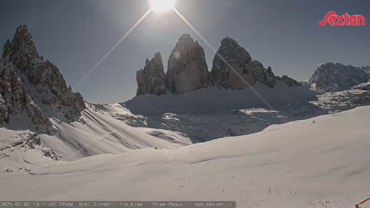 A sunny, snow-covered mountain valley with several prominent rock formations rising in the background.