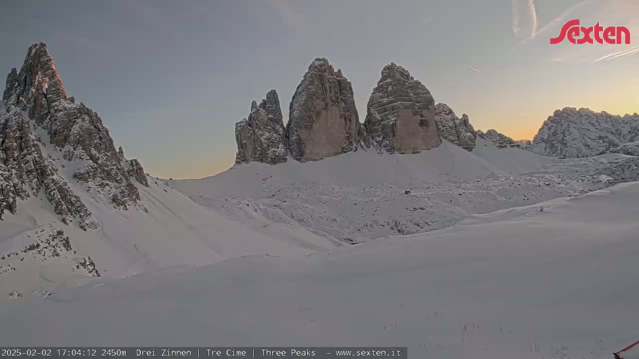 A snow-covered mountain range with prominent, tall rock formations is visible at sunset.