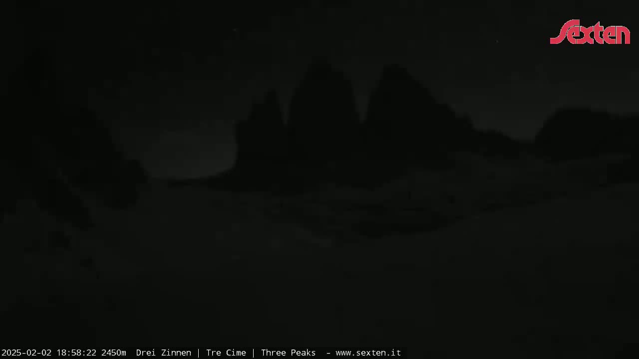 A nighttime, low-light image shows three dark, silhouetted peaks in the distance.