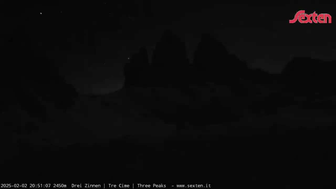 A dark, nighttime view of silhouetted mountains under a mostly clear sky.