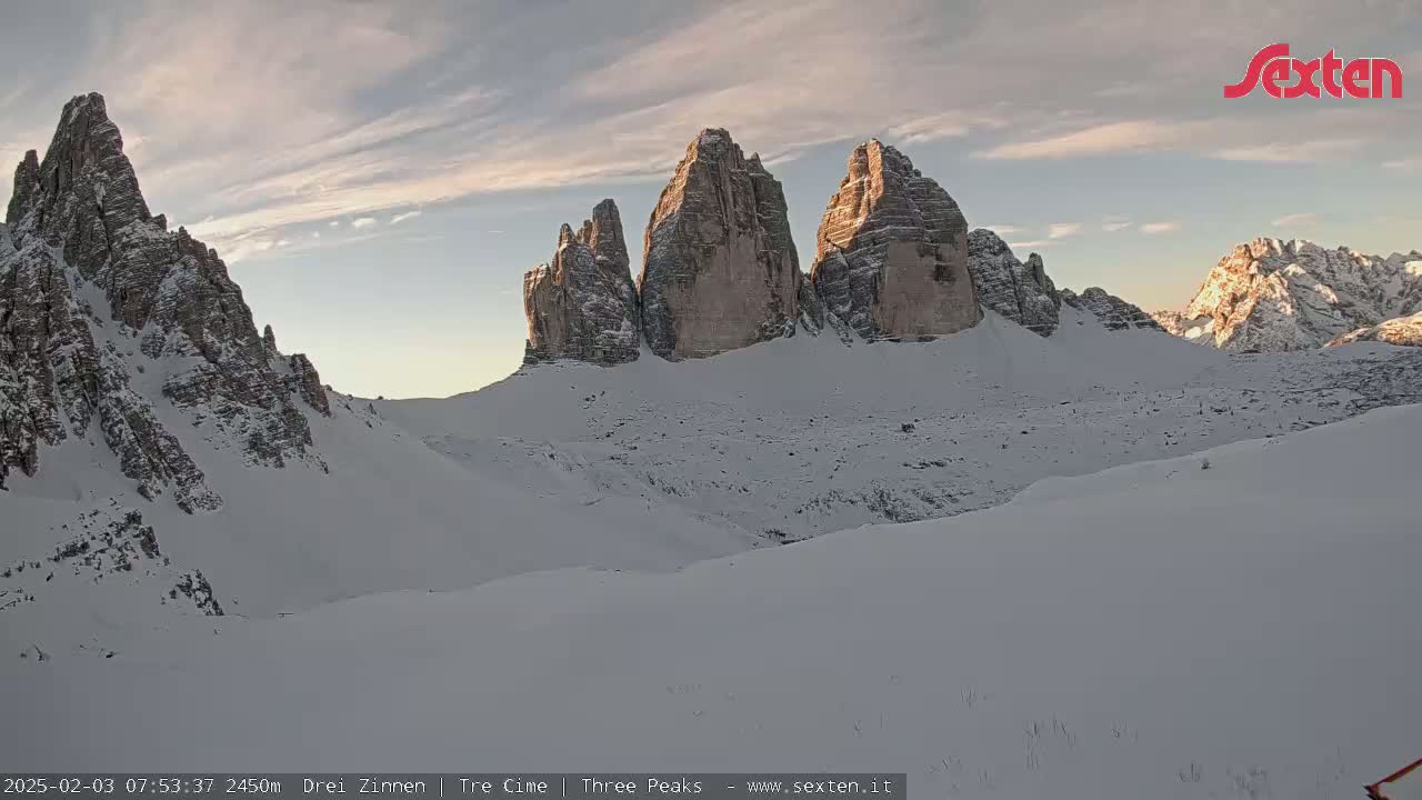 A snow-covered mountain range with several prominent, rocky peaks is visible under a partly cloudy sky.