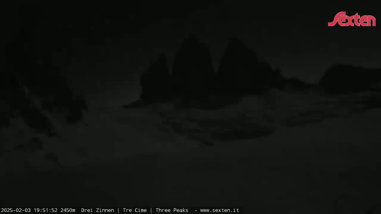 A nighttime, low-light view of three dark, indistinct mountain peaks under a cloudy sky.