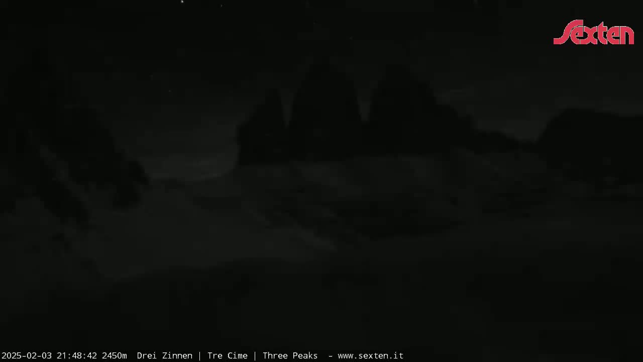 A dark, nighttime outdoor image shows a faintly visible mountain range under a mostly clear sky.