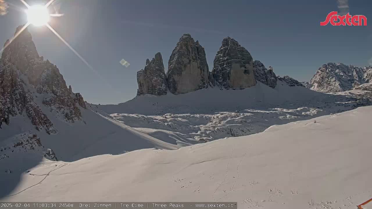 A sunny, snow-covered mountain landscape features a prominent rock formation in the background.