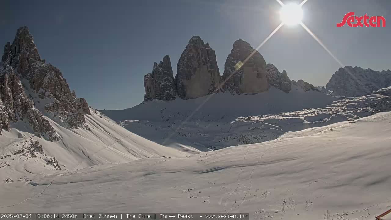 A sunny day in a snow-covered mountain valley with tall, rocky peaks in the background.