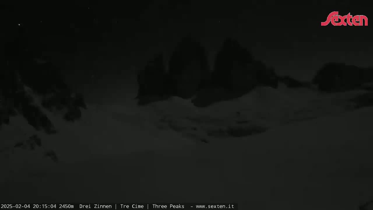 A nighttime, snowy landscape shows dark, snow-covered mountain peaks under a clear, dark sky.