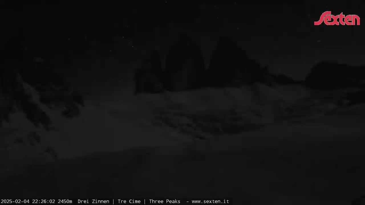 A nighttime, low-light view shows dark, snow-covered mountains under a mostly clear sky.
