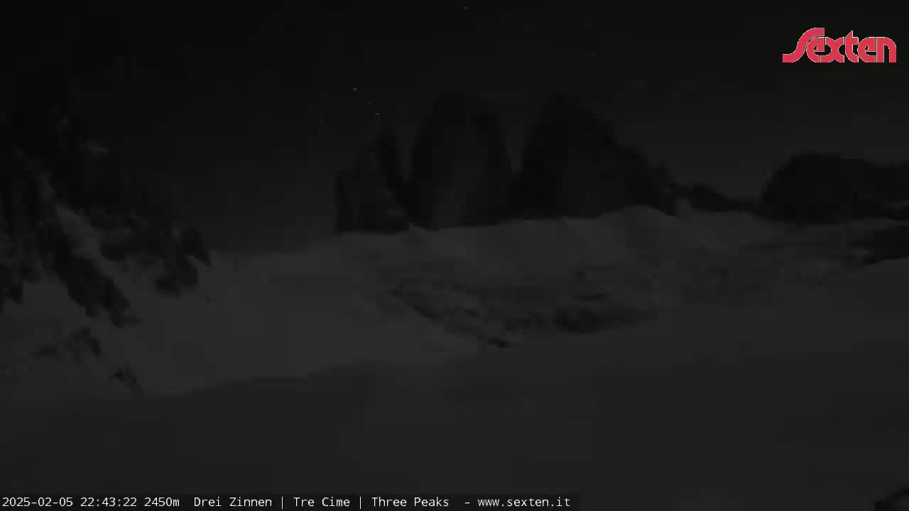 A nighttime, snow-covered landscape features dark, mountainous silhouettes under a clear, starlit sky.