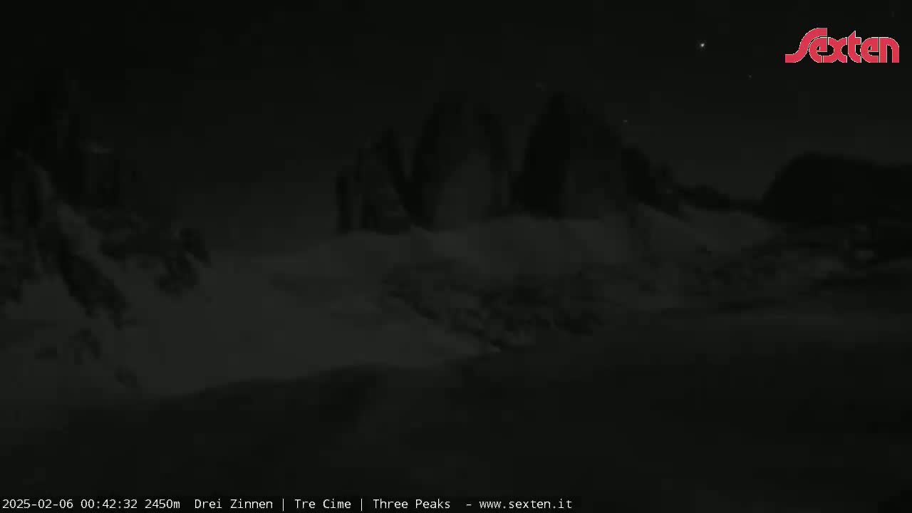 A nighttime, low-light view of dark, snow-covered mountains under a clear sky.
