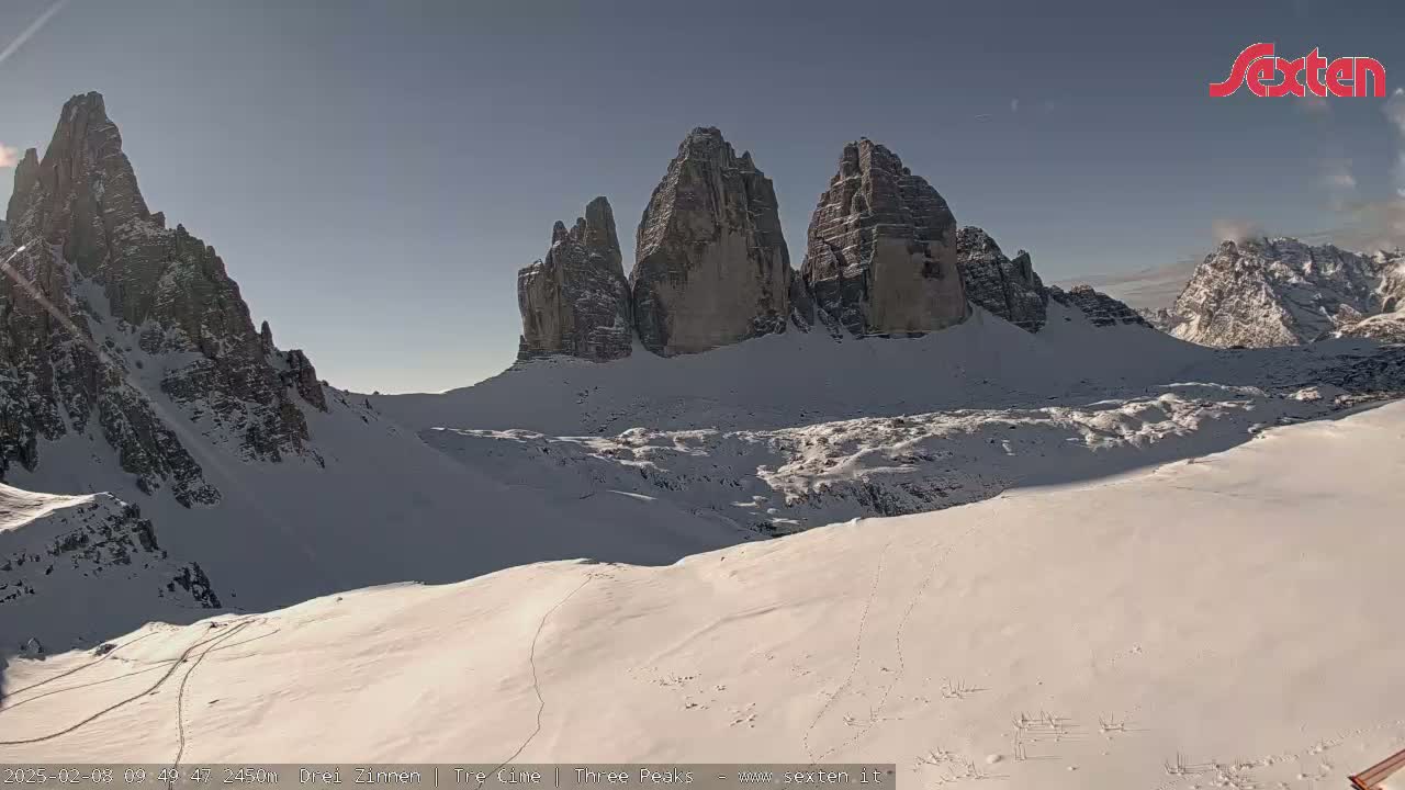 A snow-covered mountain range with prominent, tall rock formations is visible under a clear, sunny sky.