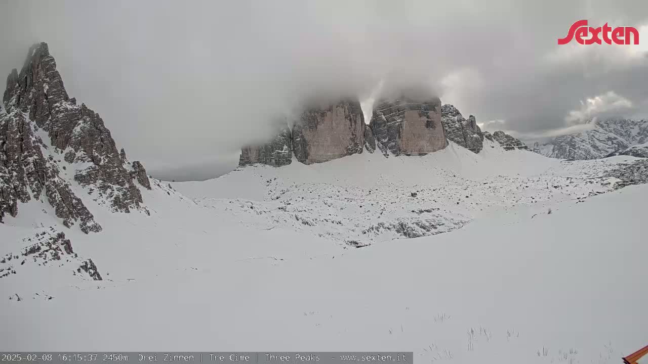 A snow-covered mountainous landscape with large rock formations partially obscured by fog.