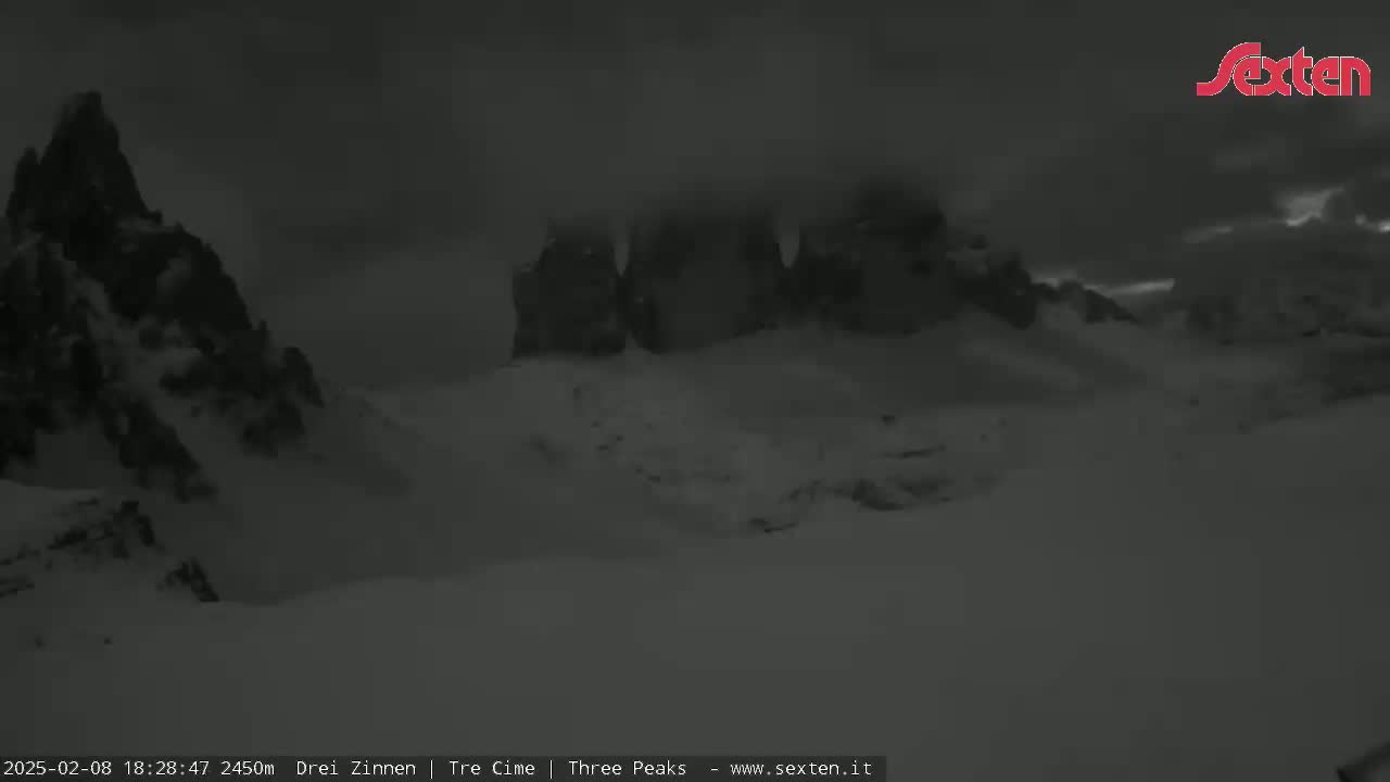 A snow-covered mountain range is partially obscured by heavy clouds at night.
