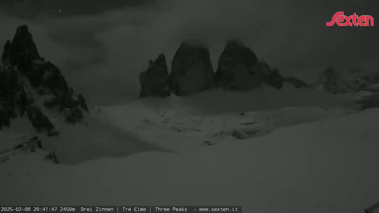 A snow-covered landscape with dark, rocky peaks shrouded in mist or fog under a dark sky.