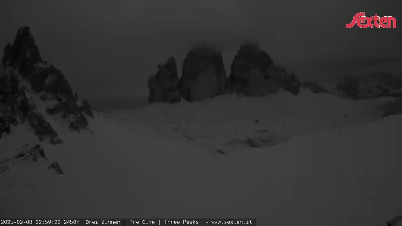 Snow-covered rocky peaks are partially obscured by a heavy fog or low-hanging clouds.