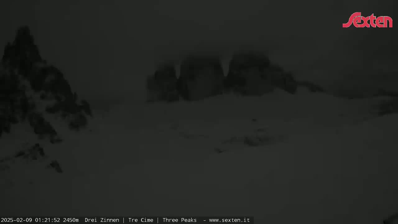 A dark, snowy landscape features several large rock formations under a dim, overcast sky.