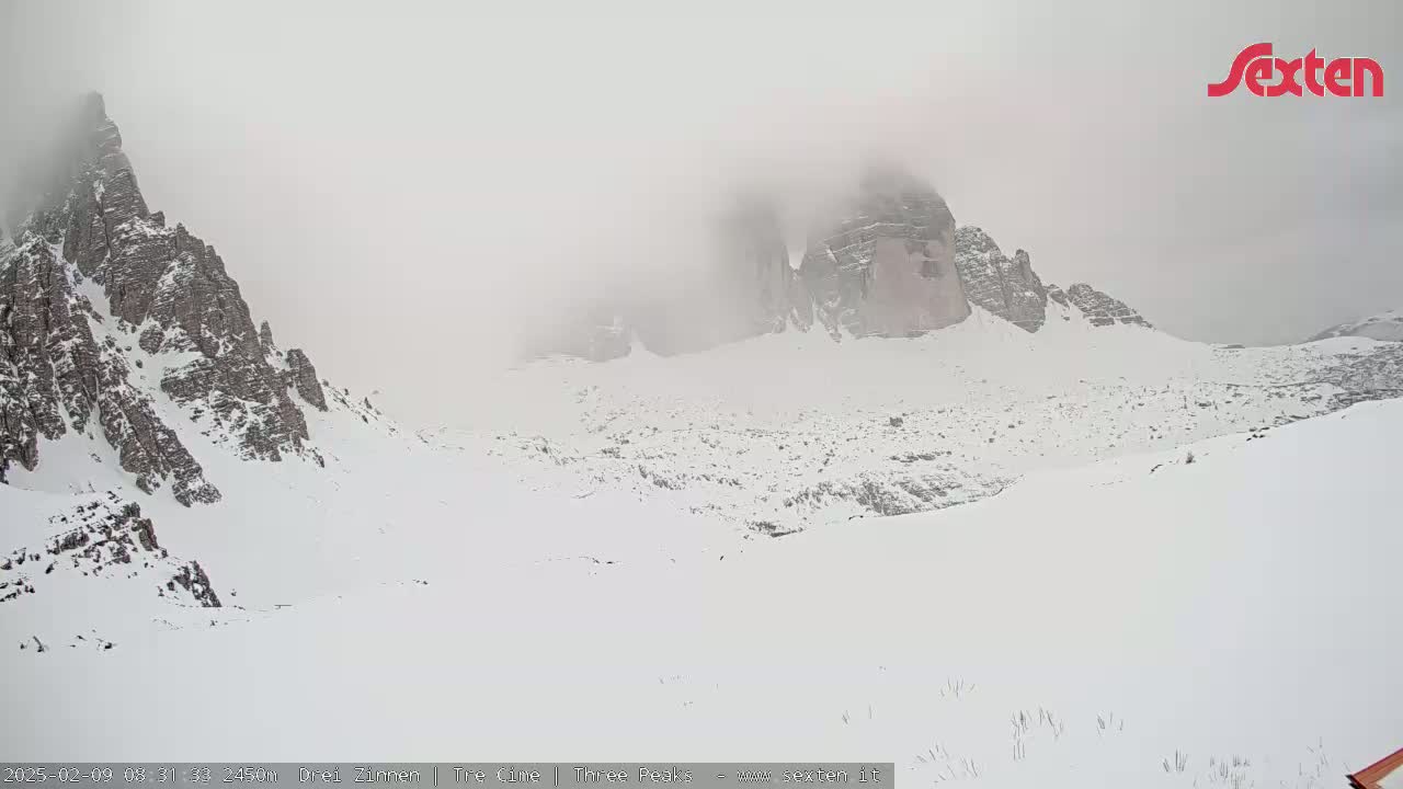 A snow-covered mountainous landscape is shrouded in fog.