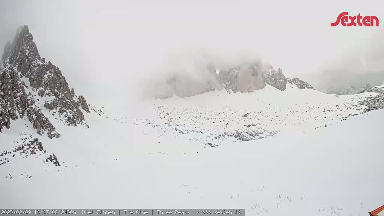A snow-covered mountain valley is partially obscured by fog, with rocky peaks visible in the background.