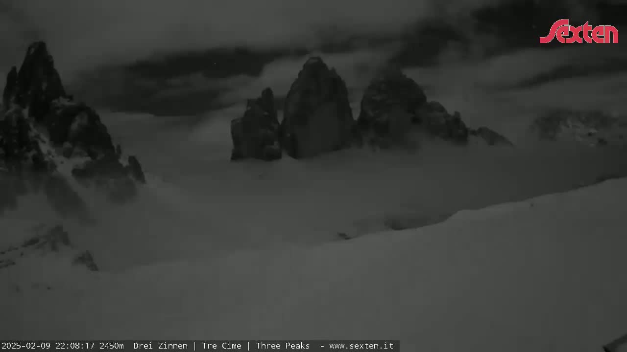 A snow-covered mountainous landscape is shrouded in low-hanging clouds under a dark sky.