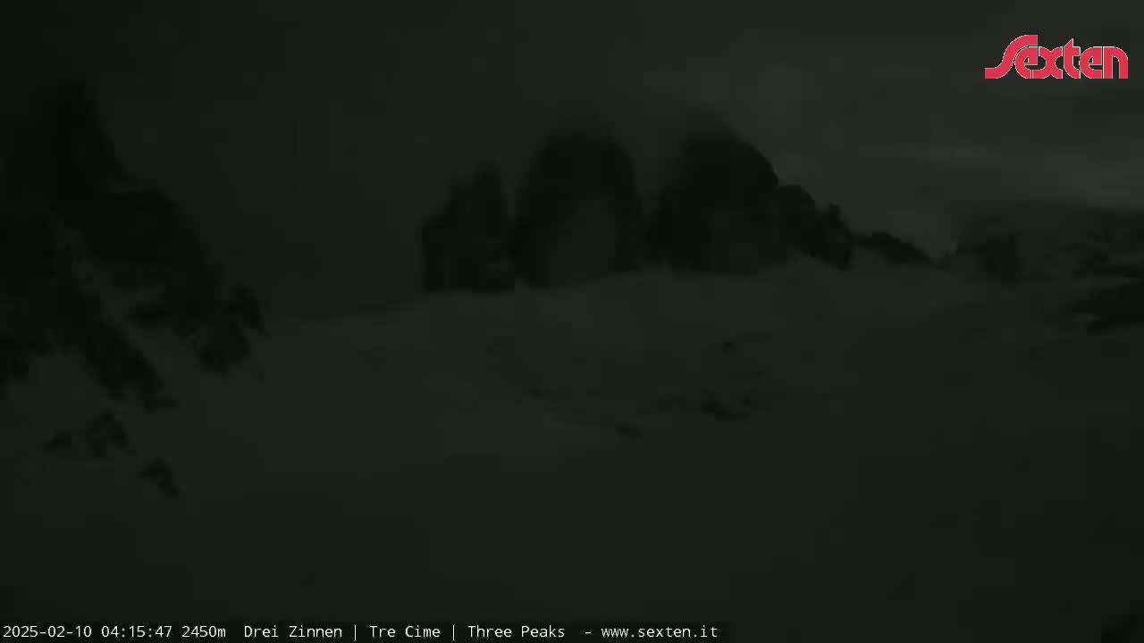 A dark, snowy landscape is visible at night, with three large, indistinct mountain peaks in the distance.