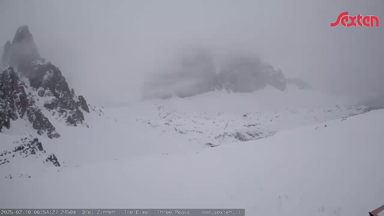A snow-covered mountainous landscape is shrouded in heavy fog or blowing snow.