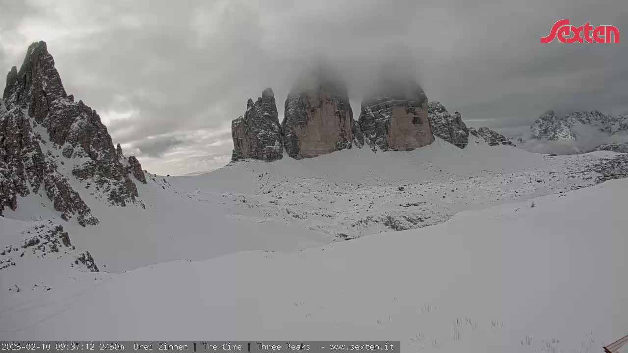 A snow-covered mountainous landscape with three prominent rock formations partially obscured by fog under an overcast sky.
