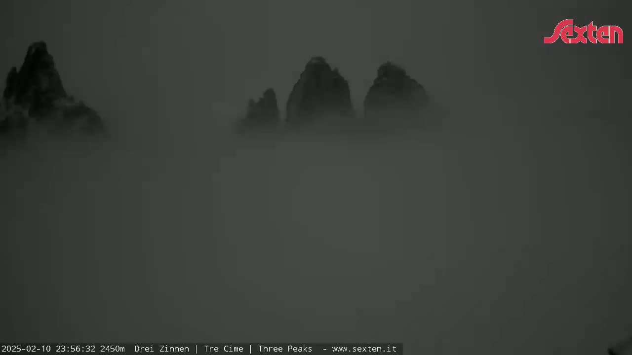 Several mountain peaks are barely visible through a thick fog.