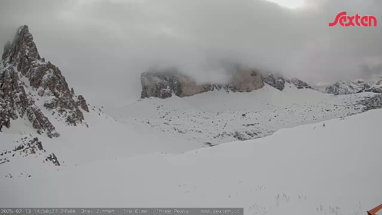A snow-covered mountain landscape is shrouded in fog, with rocky peaks partially visible.