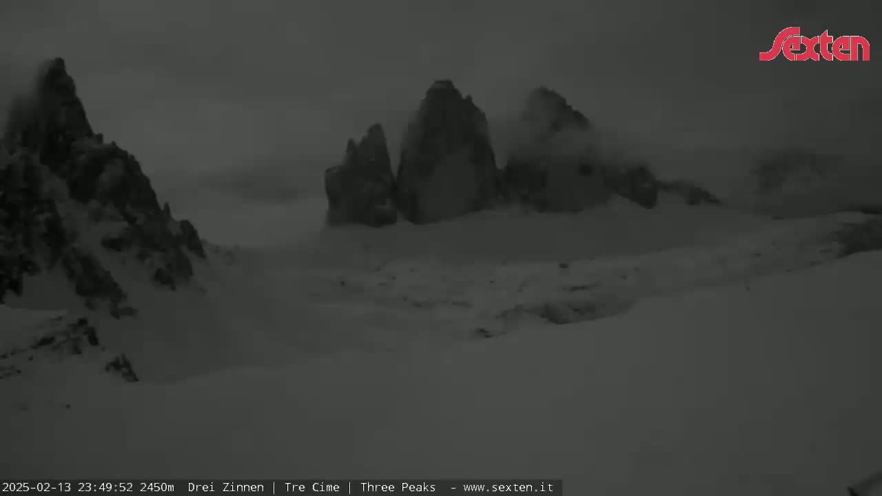 Snow-covered mountains are partially obscured by fog or low clouds in a dark, overcast setting.