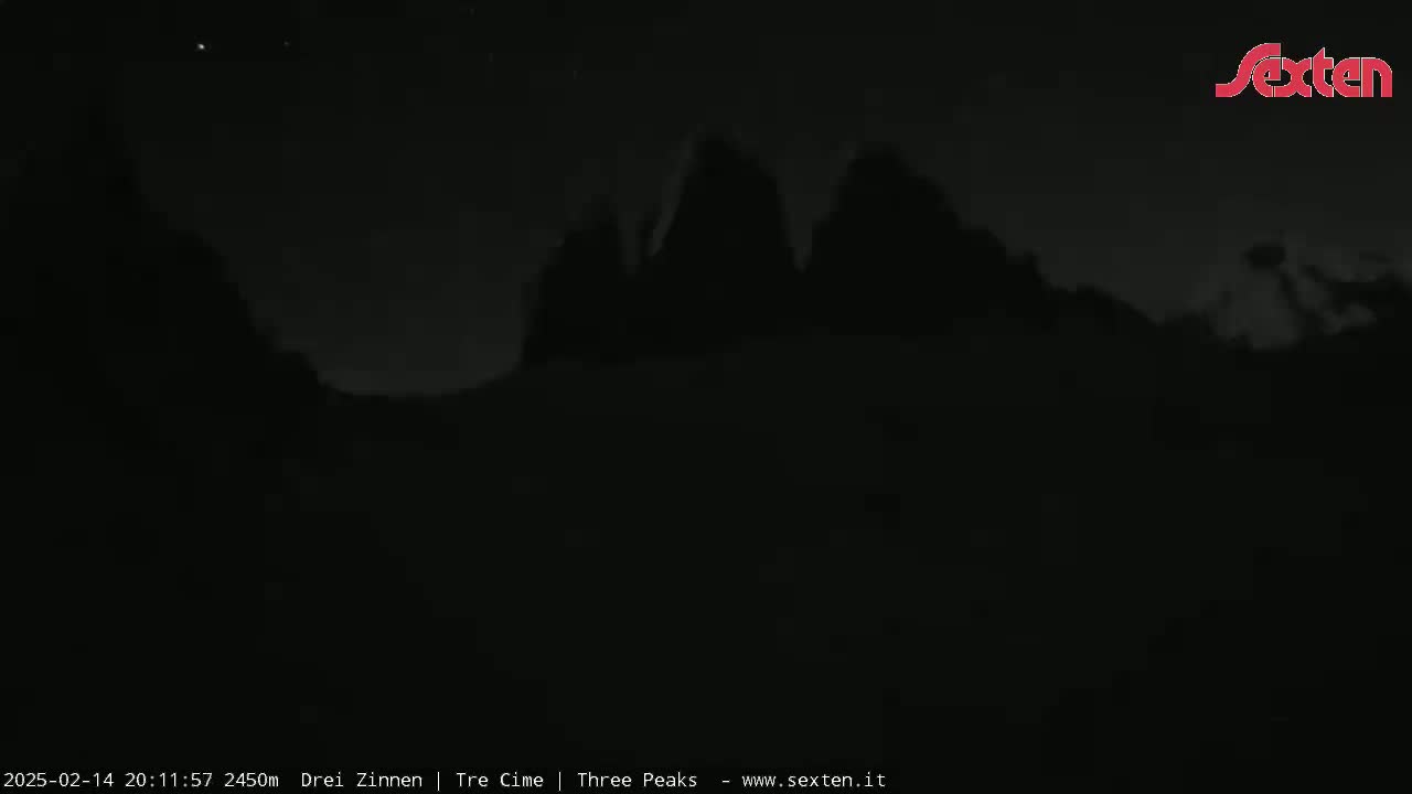 A dark, nighttime image shows three silhouetted mountain peaks under a mostly clear sky.