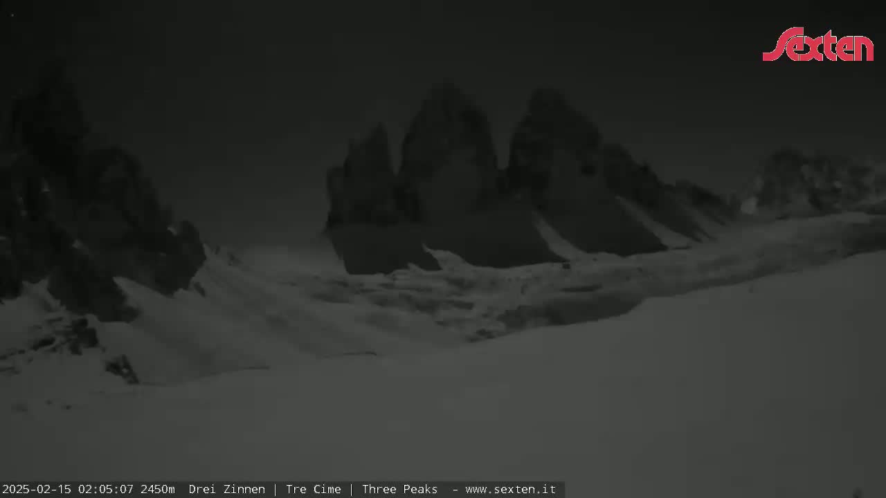 A nighttime, snow-covered landscape features a range of dark, jagged mountains under a dark sky.