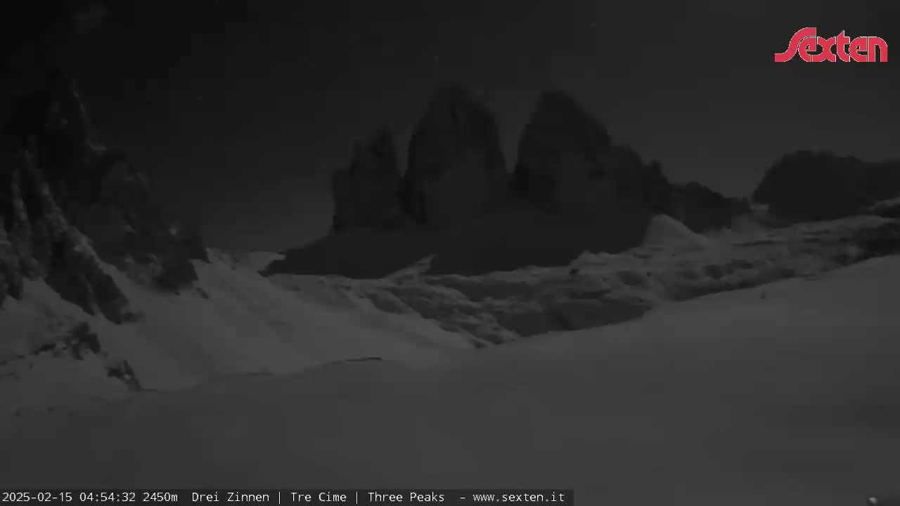 A nighttime, snow-covered landscape features a range of dark, imposing mountains under a dark sky.