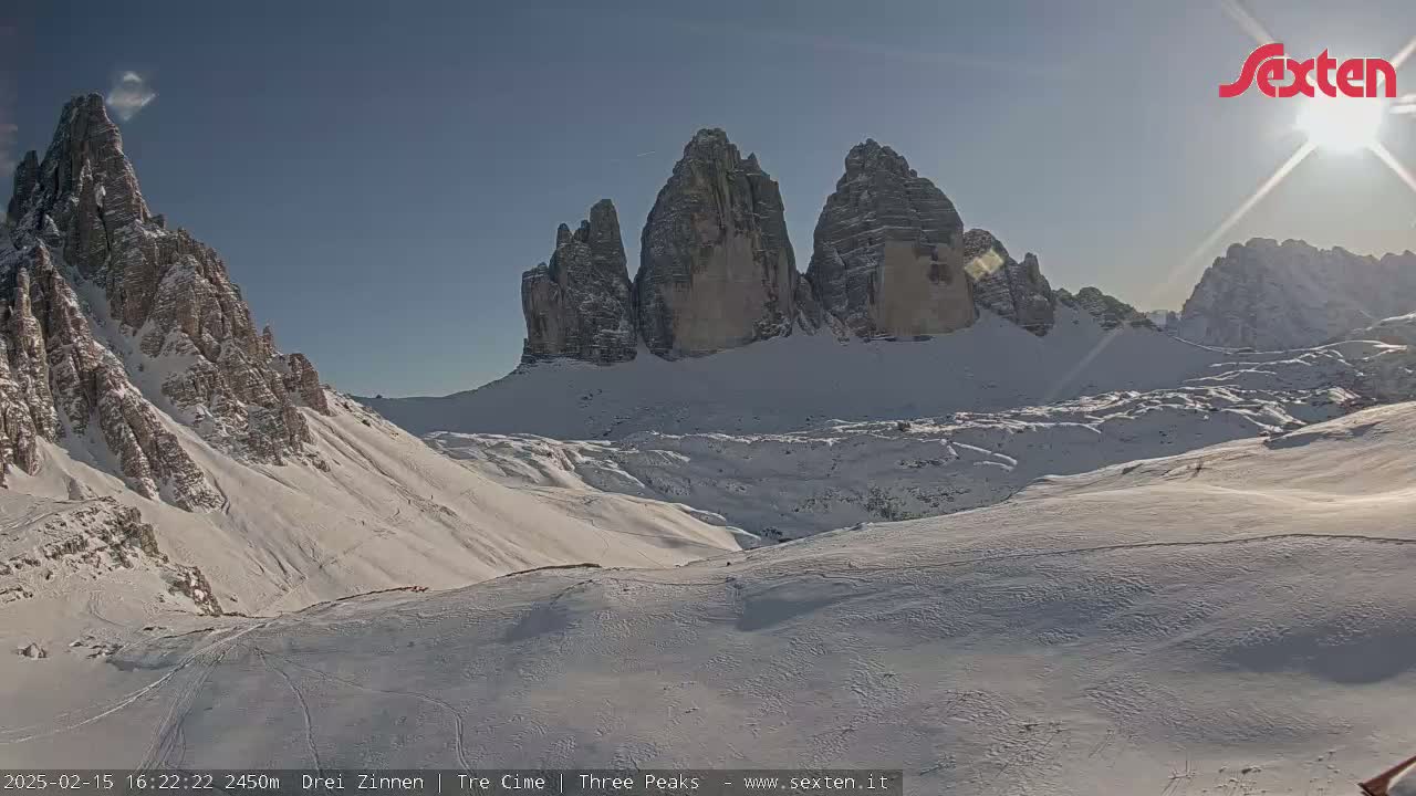 A sunny day reveals a snow-covered mountain range, with prominent, sharply peaked rock formations in the background.