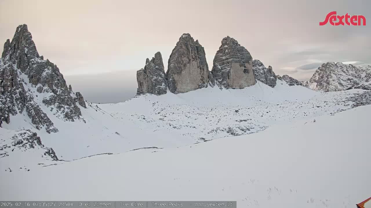 A snow-covered mountain range with several prominent rock formations is visible under a pale, overcast sky.