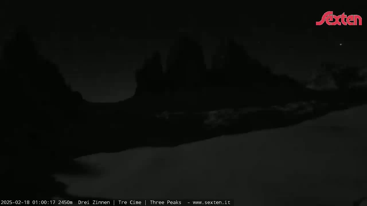 A nighttime, low-light image shows dark, silhouetted mountains under a mostly clear sky.