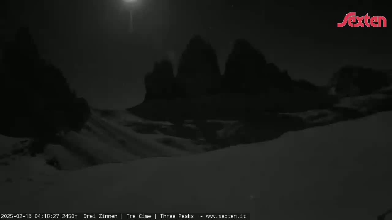 A nighttime, snow-covered landscape features three dark, rocky peaks under a bright moon.