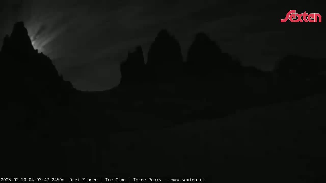 Silhouetted mountain peaks are visible under a dark, cloudy night sky with a bright light source shining from behind one of the peaks.