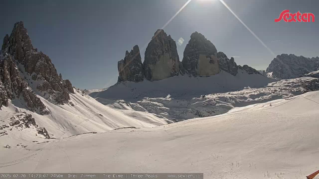 A sunny, snow-covered mountain valley with prominent rock formations in the background.