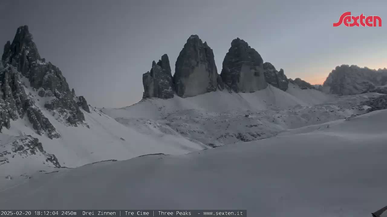 A snow-covered mountain range, with several prominent rock formations, is visible under a twilight sky.