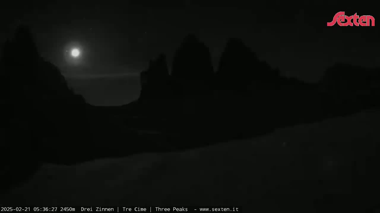 A bright moon illuminates silhouetted mountains under a mostly clear night sky.